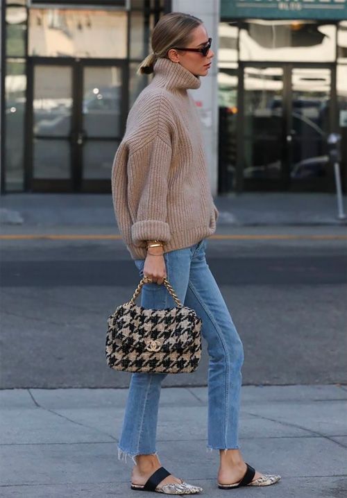 a tan oversized chunky knit sweater, blue raw hem jeans, snakeskin mules and a cozy bag