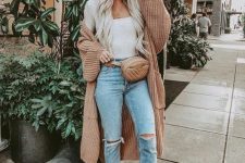 a white top, blue ripped jeans, blush booties, a tan chunky knit cardigan and a waist bag