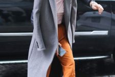 Emilia Clarke wearing a white top, rust-colored pants, tan shoes, a grey midi coat