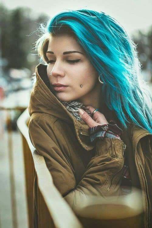 a double cheek piercing, a lip piercing and tunnel piercings plus blue hair for a super bold look