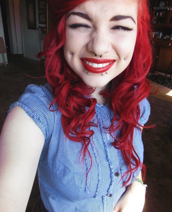 a double cheek piercing, a septum and lip piercing plus red hair to rock a very bold look