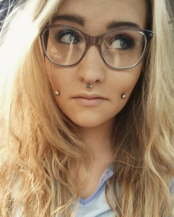 a double cheek piercing and a septum one spice up the nerdy look making it edgy and bolder