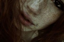 a double cheek piercing and lots of freckles accent the face a lot making it look edgy and bold