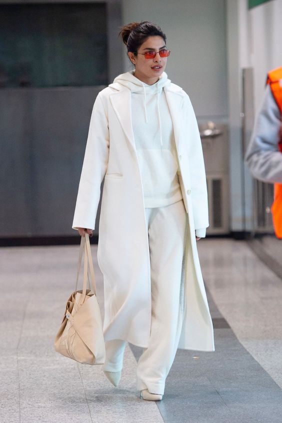 a monochromatic outfit in white, with a hoodie, pants, a midi coat and a tan bag