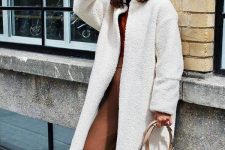a rust-colored pantsuit, a white textural coat and a tan bag with a ring for a 70s inspired look