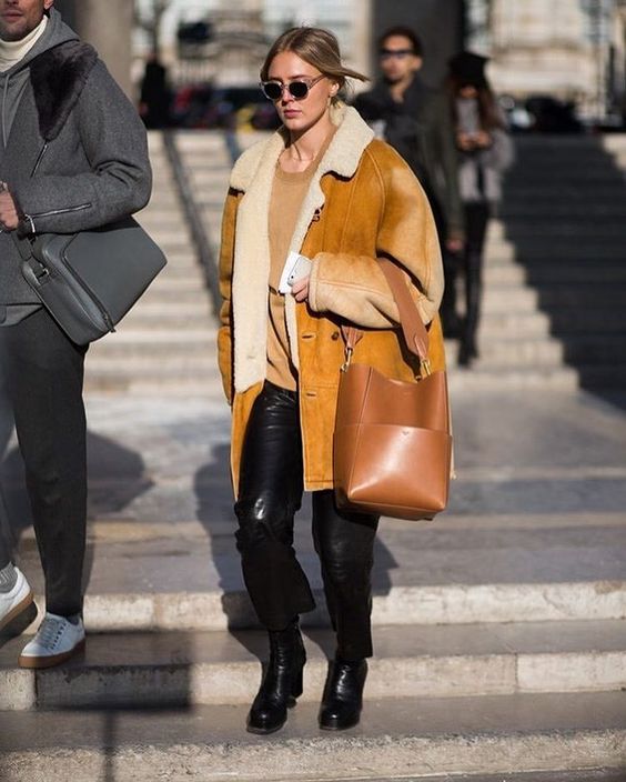 a tan top, black leather pants, black boots, an amber shearling coat and a brown bag with a minimalist handle