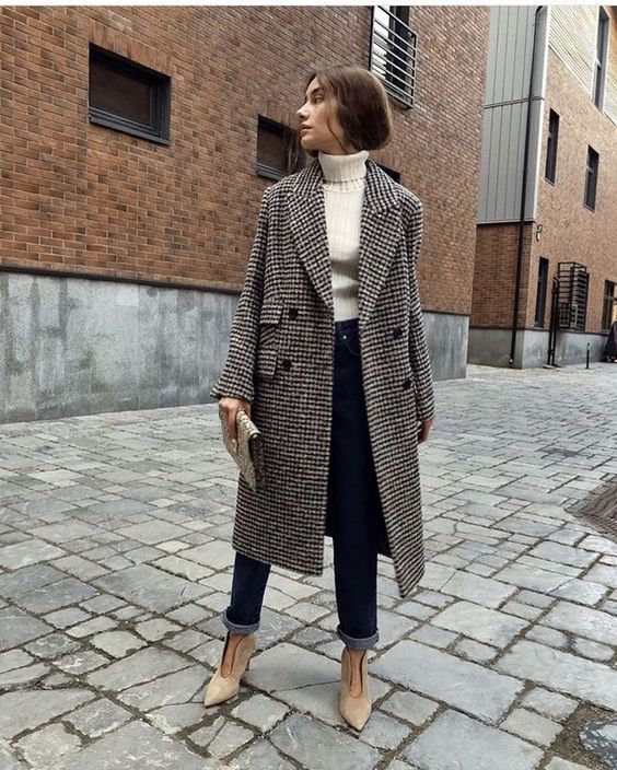 a white turtleneck, navy straight jeans, tan cutout booties, a clutch and a plaid midi coat