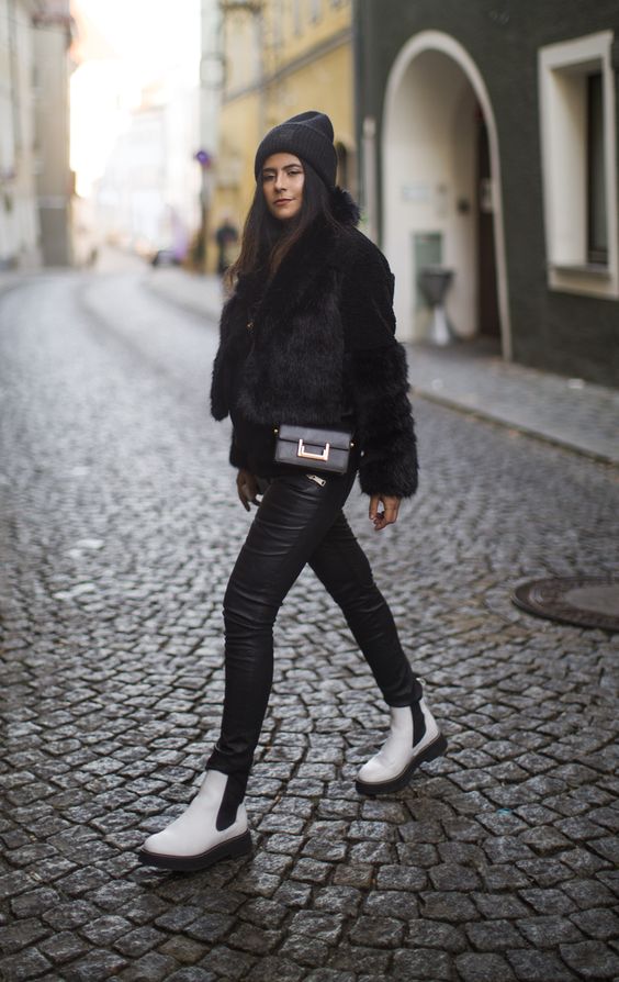 a bold and comfy winter look with a black faux fur jacket, leather leggings, white Chelsea boots, a black bag and a beanie