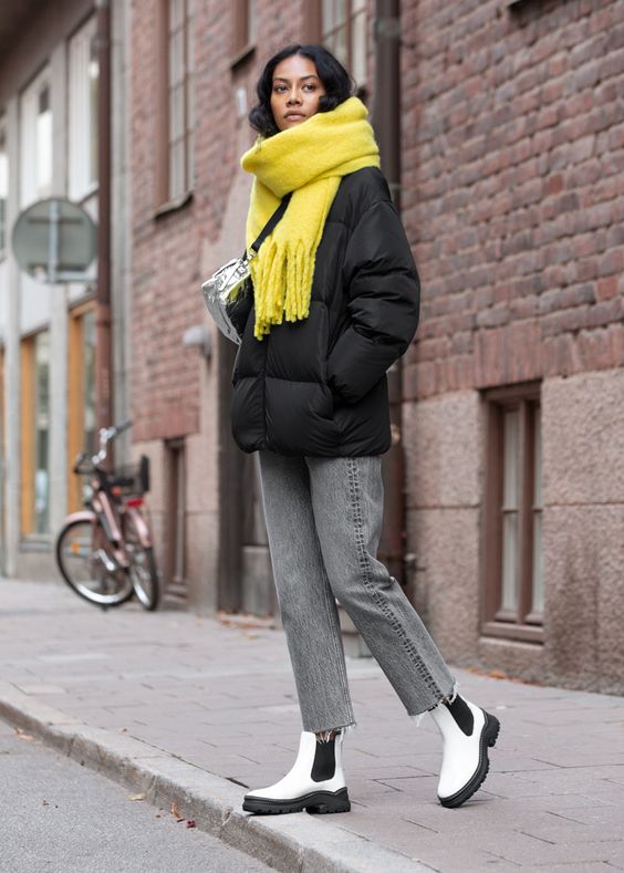 a casual yet bold winter look with a black puff jacket, grey jeans, white Chelsea boots and a lemon yellow scarf