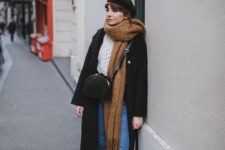 a cozy winter look with a white chunky sweater, blue jeans, a black coat and a beret, a crossbody bag, mustard shoes and an oversized tan scarf