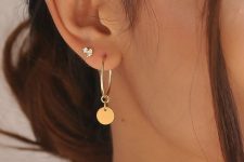 a large gold hoop earring with a coin hanging on it and a tiny embellished stud look chic together