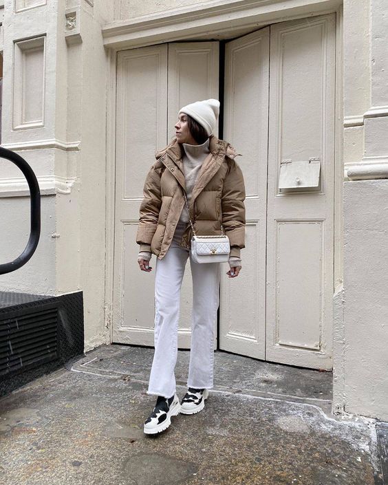 a simple and comfortable winter look with a white sweater, jeans, hiking boots, a tan leather puffer jacket and a white beanie and bag