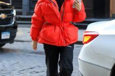 a sporty winter look with a black turtleneck, joggers, white trainers, a red puffer jacket with a belt and cap