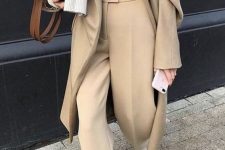 a stylish winter work look with tan pants, white boots, a white turtleneck, a grey sweater and a tan coat plus a brown bag