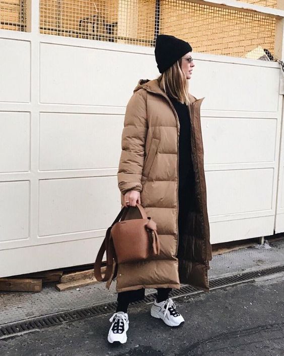 a total black look with a top and pants, a black beanie, an ocher puffer coat, a brown bag and white trainers
