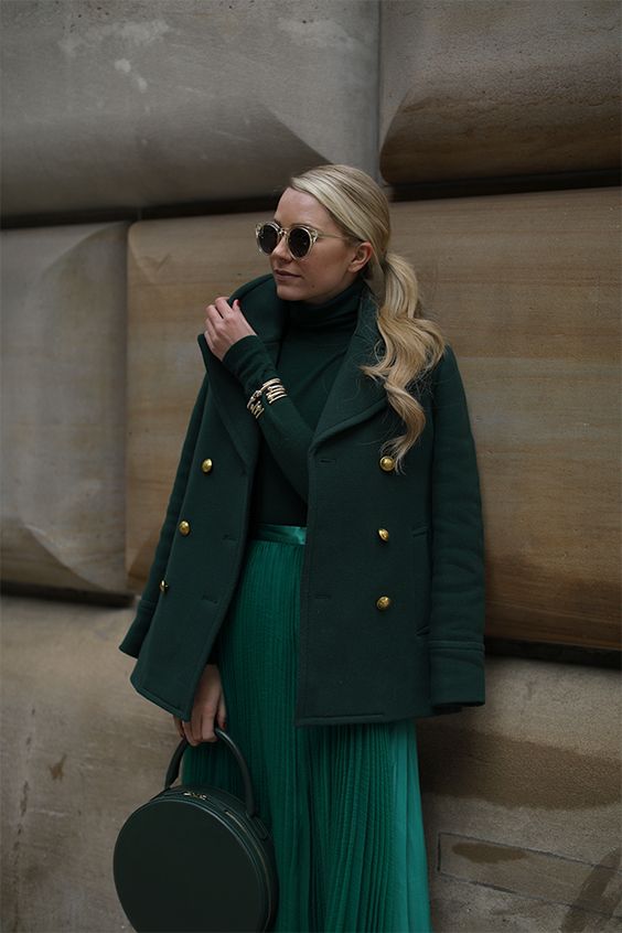 a total green look with a sweater, a metallic pleated midi, a short coat, a round bag and gold touches