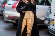 a trendy outfit with a black turtleneck, tan cargo pants, black Chelsea boots, a midi coat and a bag