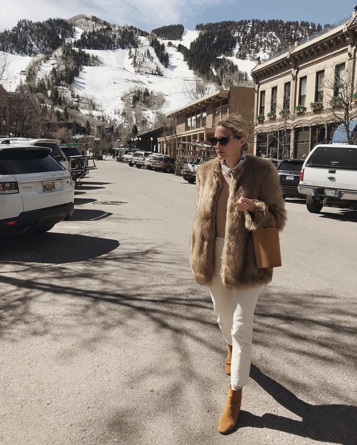 a white shirt, a tan sweater, white jeans, mustard booties, a tan faux fur jacket and a mustard bucket bag