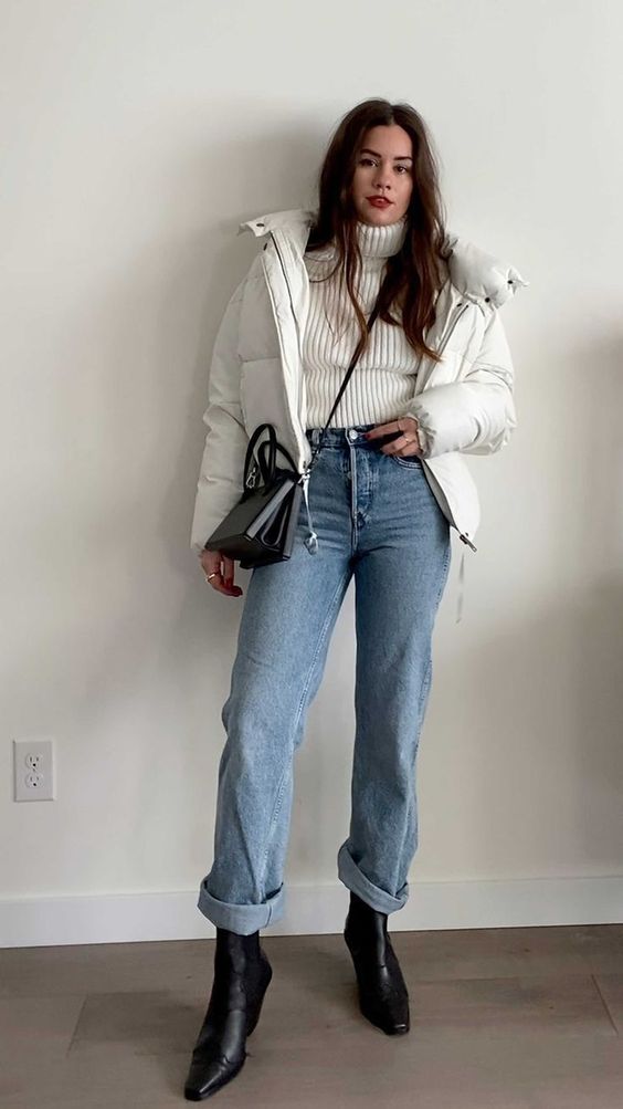 a white turtleneck sweater, blue jeans, black square toe boots, a white puffer jacket and a black bag