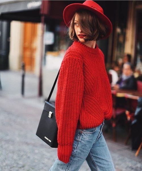an oversized red chunky knit sweater, blue jeans, a red hat, a black bag and red lips