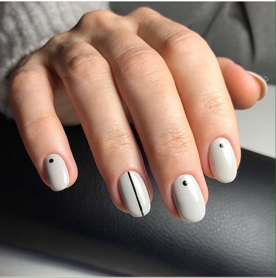 a white manicure combining dots and stripes in black is a cool modern classics to try