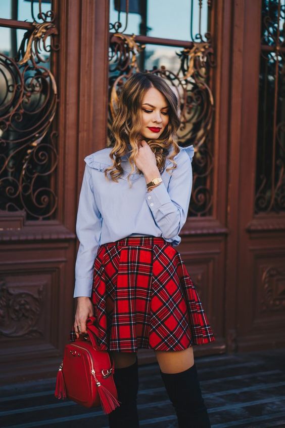a blue shirt with ruffle detailing and long sleeves, a red plaid mini skirt, a red bag and black thigh boots