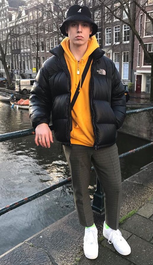 a bold and trendy look with a yellow hoode, a black puffer jacket, grey plaid pants, bright socks and white trainers, a bucket hat