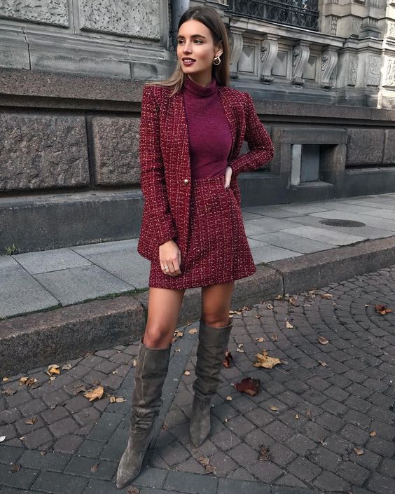 a bold work outfit with a red tweed skirt suit, a purple turtleneck, grey knee-high boots and statement earrings