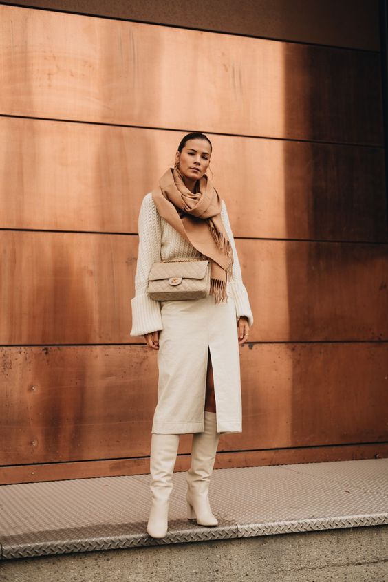 a total white outfit with a chunky sweater, a midi skirt with a front slit, white boots, a tan bag and a camel scarf