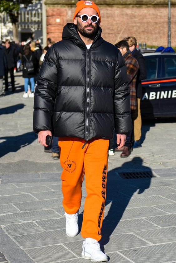 orange joggers, white trainers, an orange beanie, a black puffer jacket with a hood