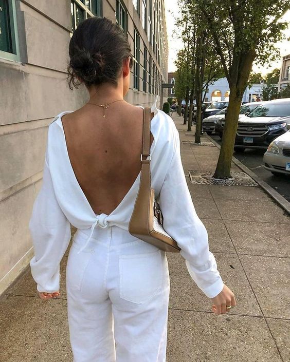 a simple look with white jeans, a white open back top with a tie and long sleeves and a baguette bag