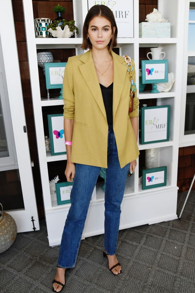 a black top, blue straight jeans, a mustard oversized blazer, black heels and a bag with a colorful chain
