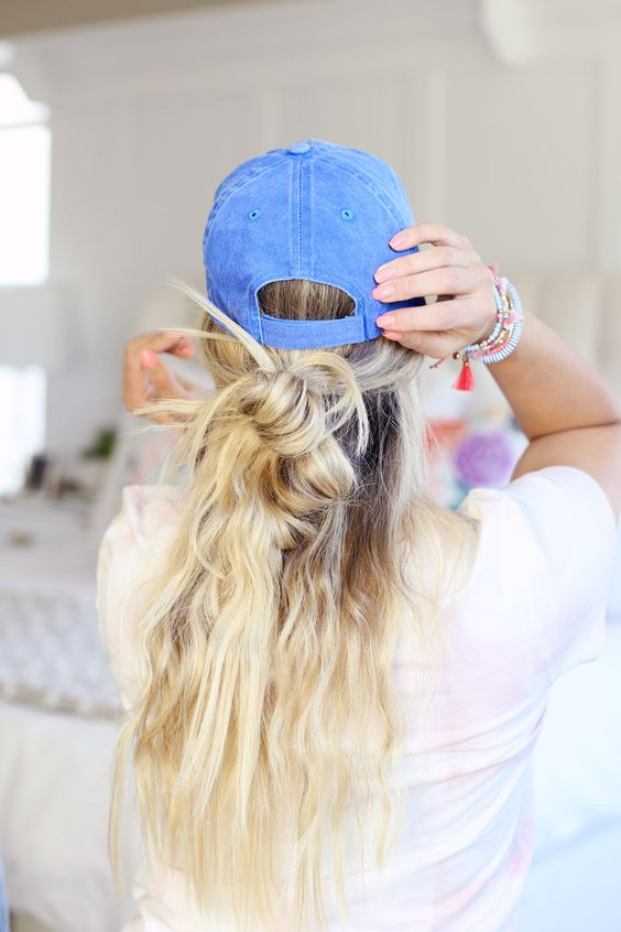 a messy half updo with messy waves and a bun plus a denim cap on top are a cool idea