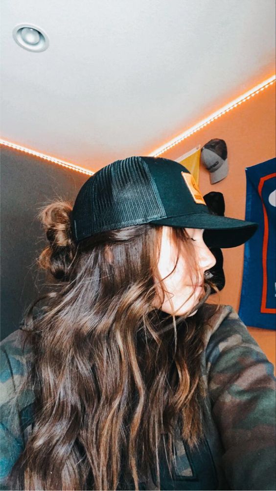 a messy wavy half updo with a midi bun and a black baseball cap on top are a super cool and catchy combo