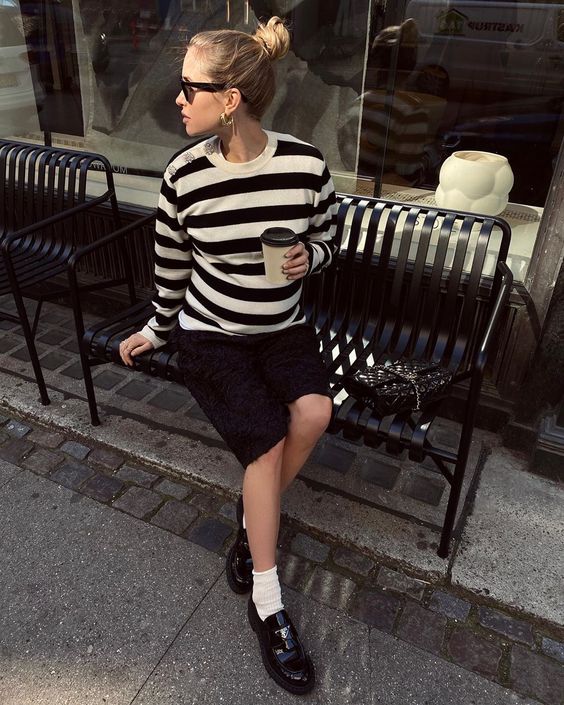 a monochromatic outfit with a striped long sleeve top, a black denim skirt, white socks and chunky loafers