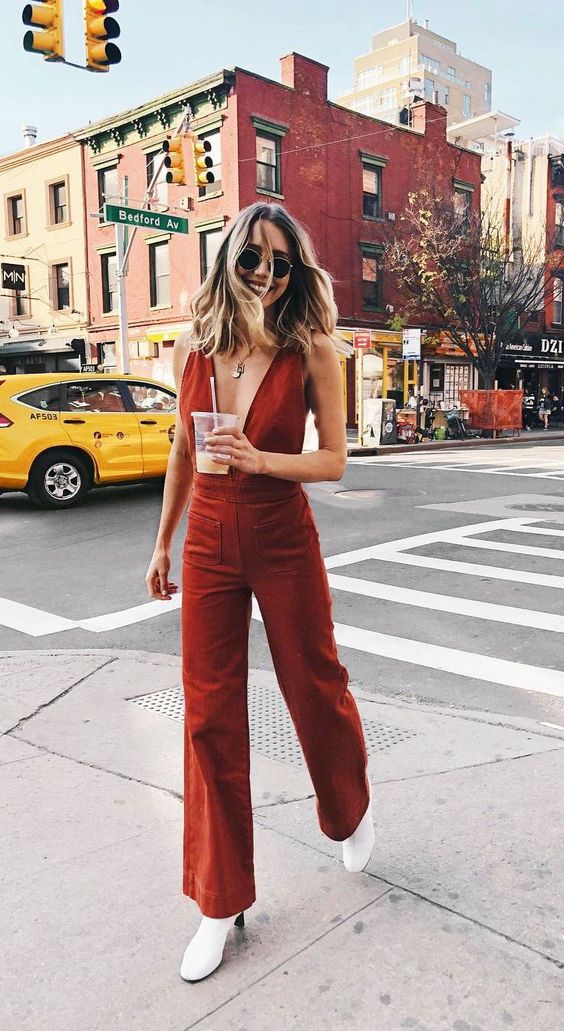 a red jumpsuit with a plunging neckline, no sleeves, mini pockets, white booties and a necklace