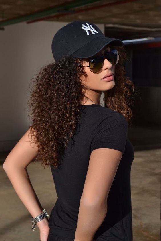 two curly low ponytails paired with a black baseball cap are a lovely hairstyle to rock anytime