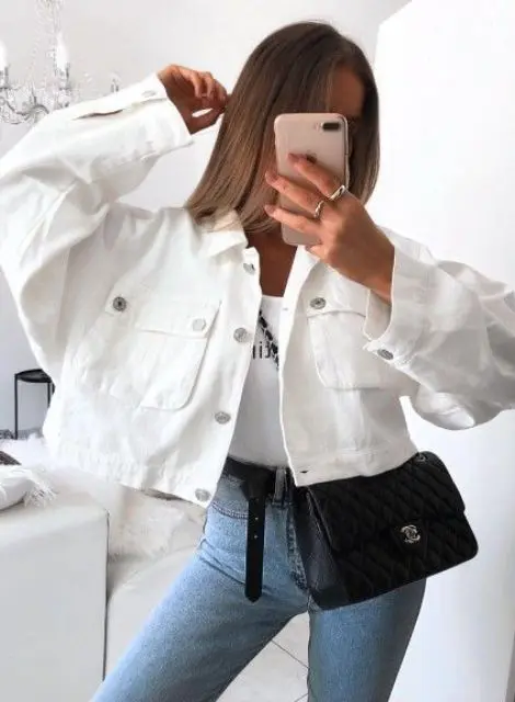 blue skinnies, a white printed top, an oversized cropped white denim jacket and a black bag