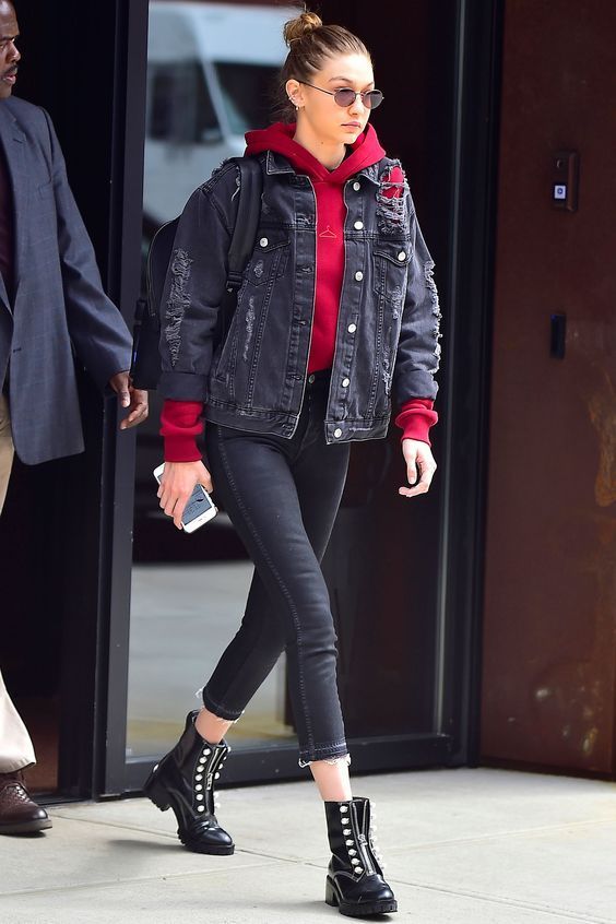 Gigi Hadid wearing a red hoodie, a black ripped denim jacket, cropped jeans, black boots and a backpack