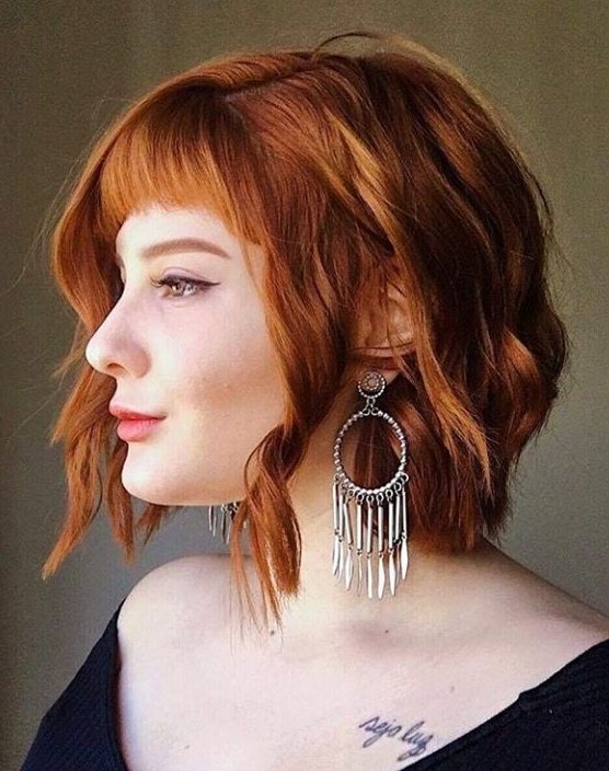 a copper red shaggy wavy bob with a classic fringe and a bit of volume is a bold and chic idea