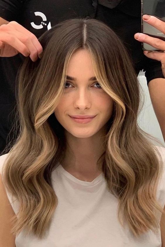 Long brunette hair with blonde balayage and face framing highlights, with volume and waves is a catchy and chic idea