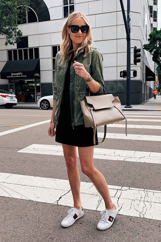 a black mini dress, a green army jacket, whiet sneakers and a tan tote plus chic sunglasses