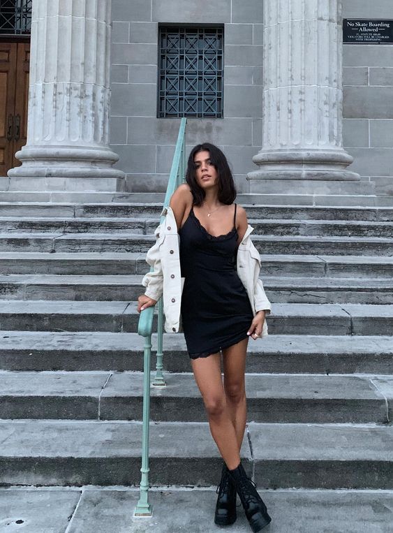 a black slip mini dress with a white denim jacket and black boots for a chic and bold look