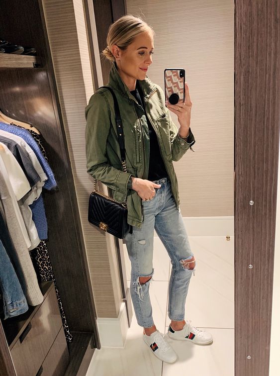 a black t shirt, ripped light blue jeans, a green army jacket, white sneakers and a black bag