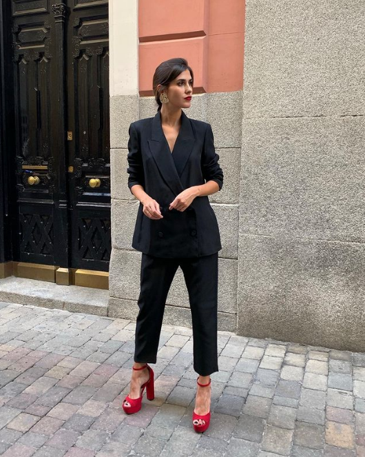 a super stylish work outfit with a black pantsuit with an oversized blazer, cropped pants, red platform shoes, statement earrings and a red lip