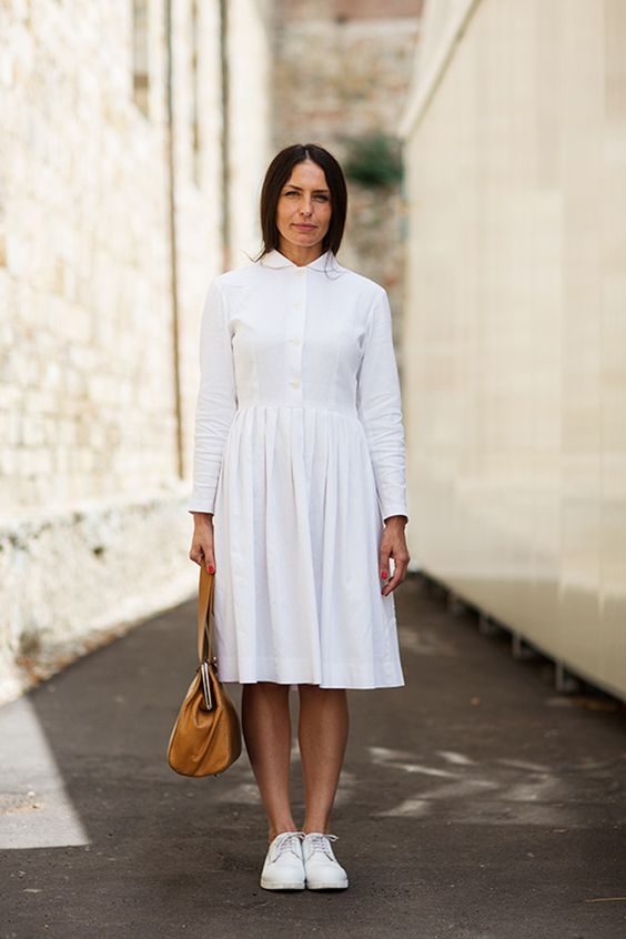 a white shirtdress with an A-line skirt and long sleeves, white sneakers and an amber bag