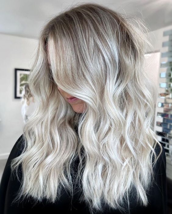 long and volumetric silver blonde hair with a darker root, messy waves is a chic idea, it looks shiny and pretty