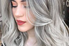 medium-length silver blonde hair with a black root, volume and waves looks adorable and super chic