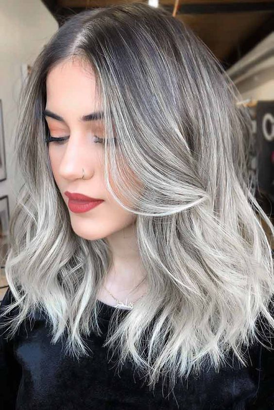 Medium length silver blonde hair with a black root, volume and waves looks adorable and super chic