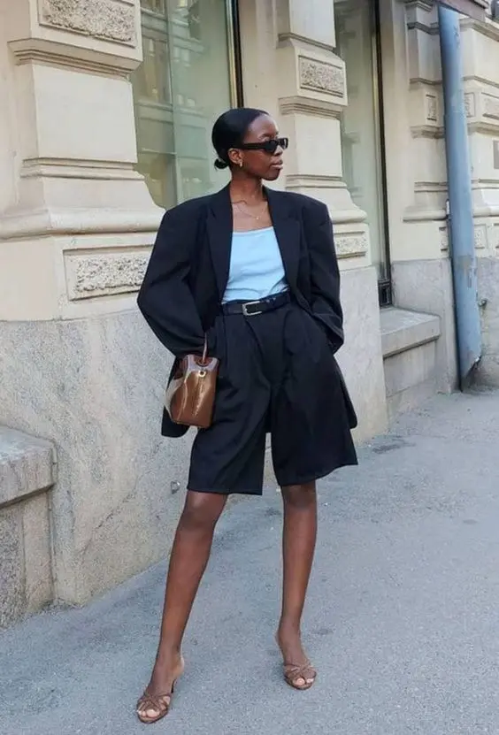 a black Bermuda short suit with an oversized blazer, a light blue top, nude heels and a brown bag